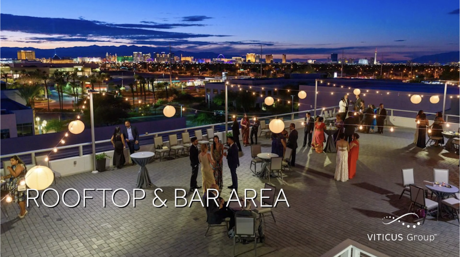 Ariel view of the Viticus Center Eastern Center rooftop bar area with people conversing in small groups. Clark County, Nevada can be seen illuminated in the distance.